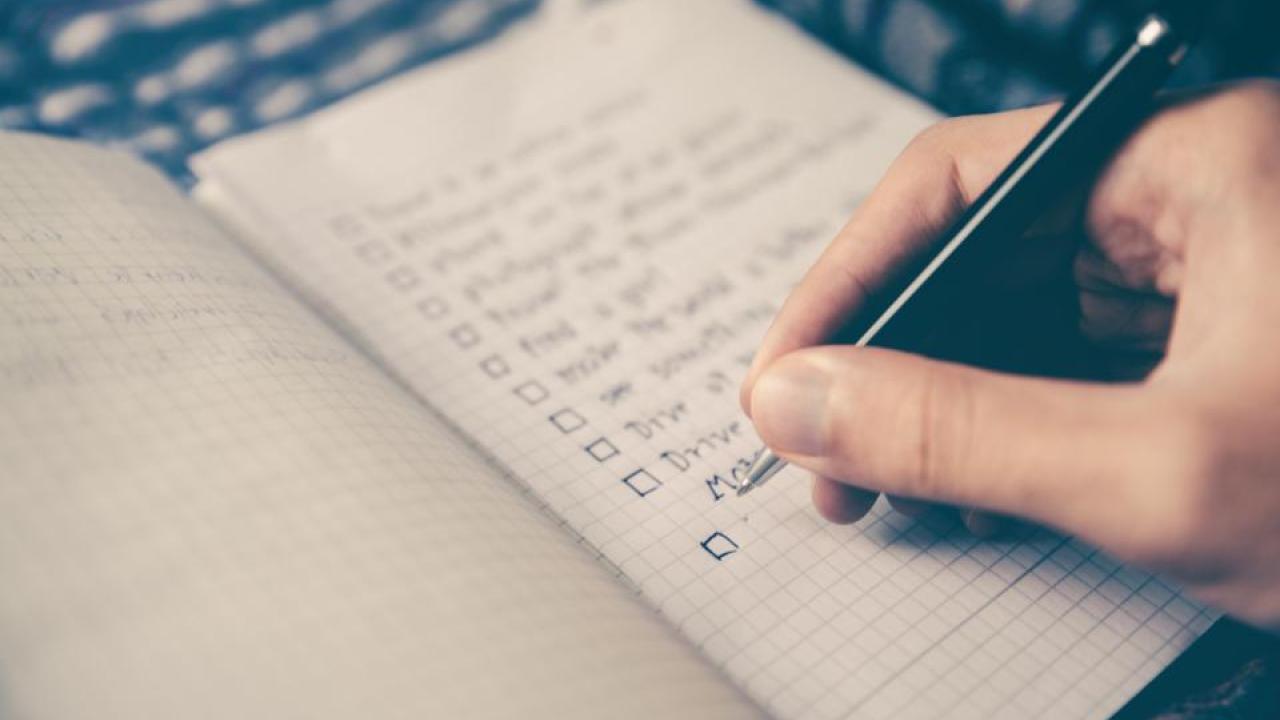 Person's hand writing a checklist with pen.